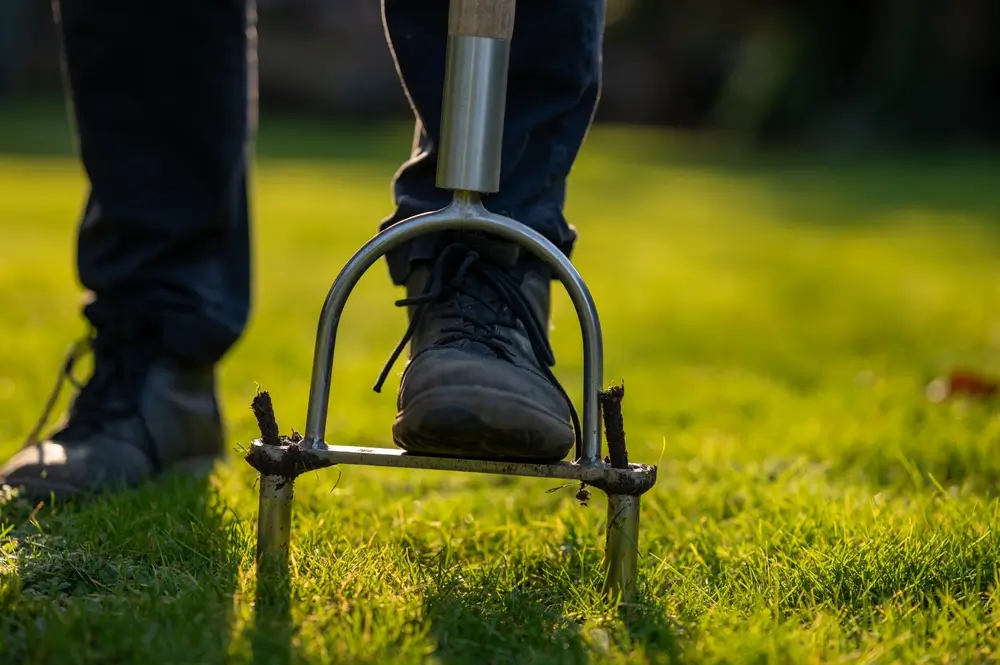 Man uses a hand aerator to fix a lawn in Wembley